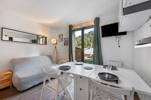 Une pièce de taille modeste comprenant une table à manger, des chaises, un canapé, un miroir et une fenêtre donnant sur une forêt.