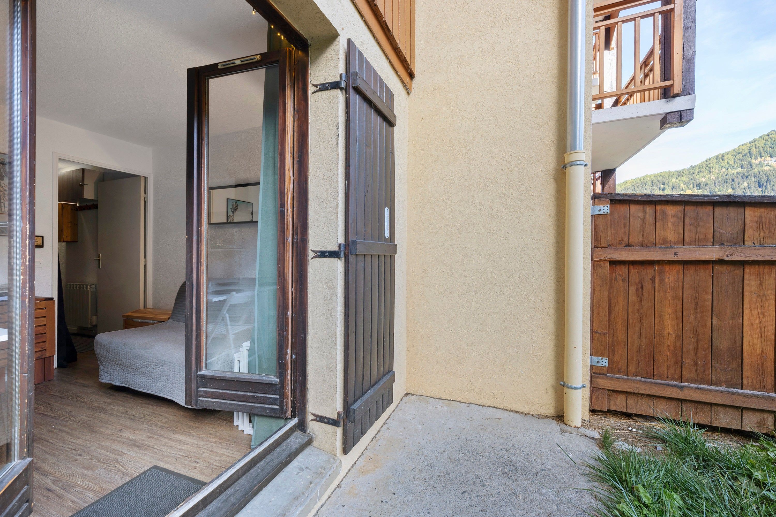 A room with a bed, a door, and a view of a wooden fence and a mountain.