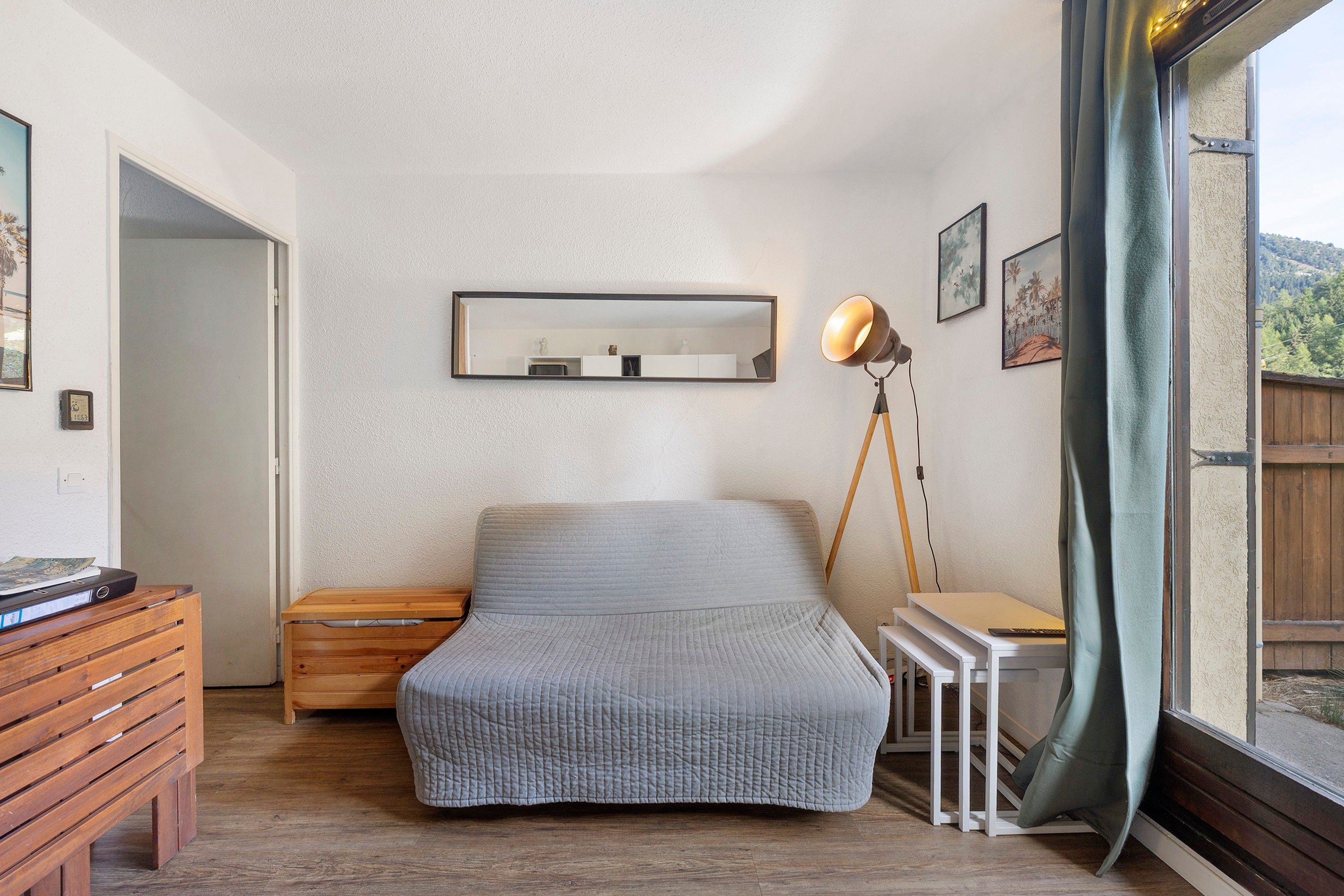 A bedroom with a bed, bedside table, lamp, and a window with curtains.