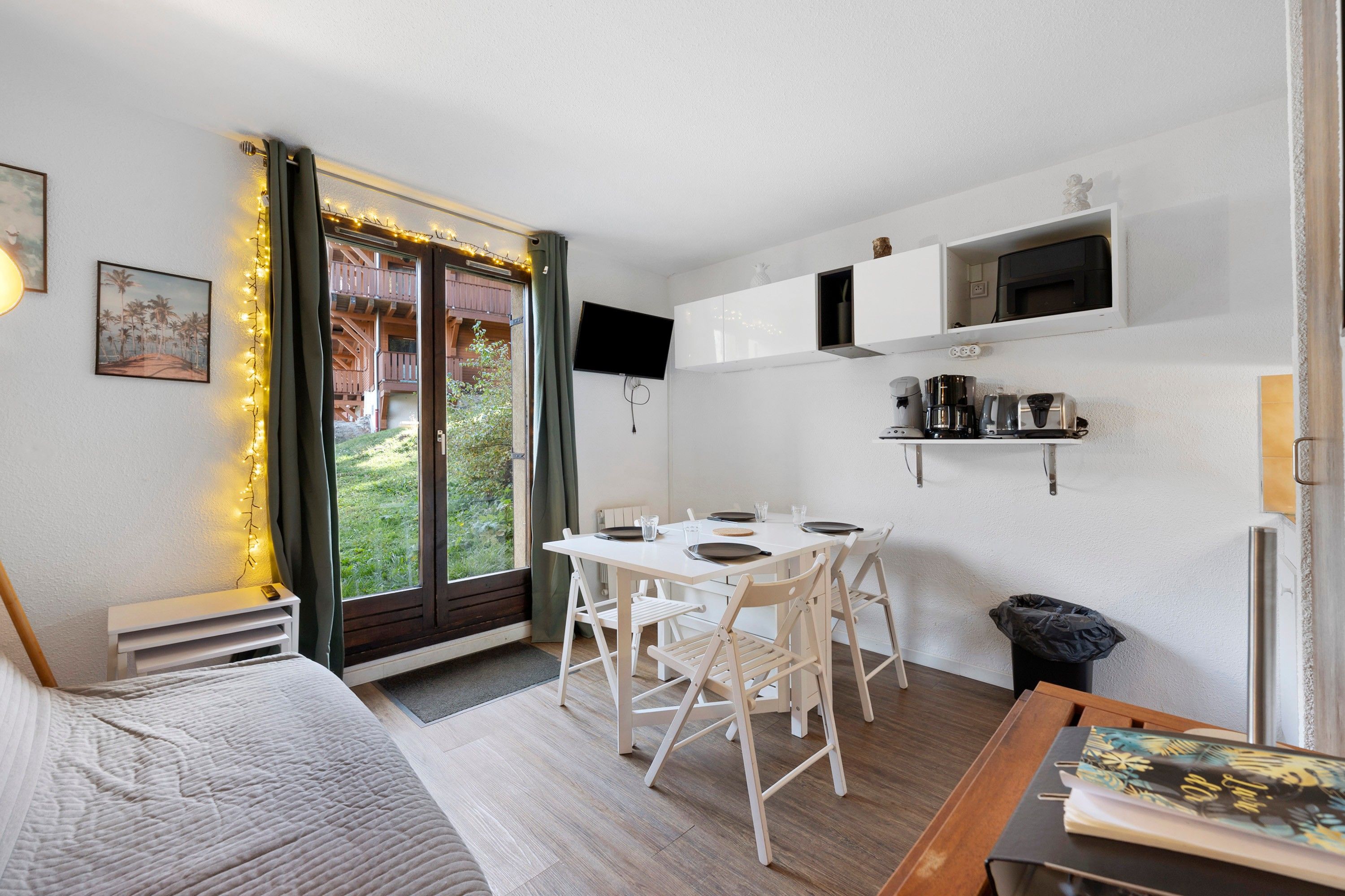 Un espace de vie compact comprenant un coin repas, un téléviseur fixé au mur et une petite kitchenette.