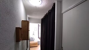 A narrow hallway with a radiator, a wooden cabinet, a door, and a dark curtain. - Studio Apartment 'Le Refuge Douillet' with Mountain View and Private Terrace (La Plagne Tarentaise)