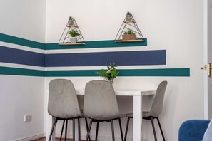 Ein Essbereich mit einem weißen Tisch, drei grauen Stühlen und zwei an der Wand befestigten Regalen mit Pflanzen.