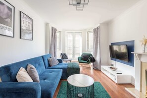 Ein Wohnzimmer mit einem blauen Sofa, einem grünen Sessel, einem Fernseher und einem Kamin.
