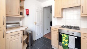 A kitchen with wooden cabinets, a gas stove, a trash bin, and a door leading to another room. - Spacious Apt Stay - Near City Centre & Tram -Walk to Leith (Edinburgh)