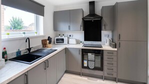 A modern kitchen with a black sink, white appliances, grey cabinets, and a window with a view. - Spacious 6-Bed Home for 9, Free Parking, Nr Centre (Newcastle)