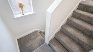 A staircase with carpeted steps and a window with a vase of dried flowers. - Spacious 6-Bed Home for 9, Free Parking, Nr Centre (Newcastle)