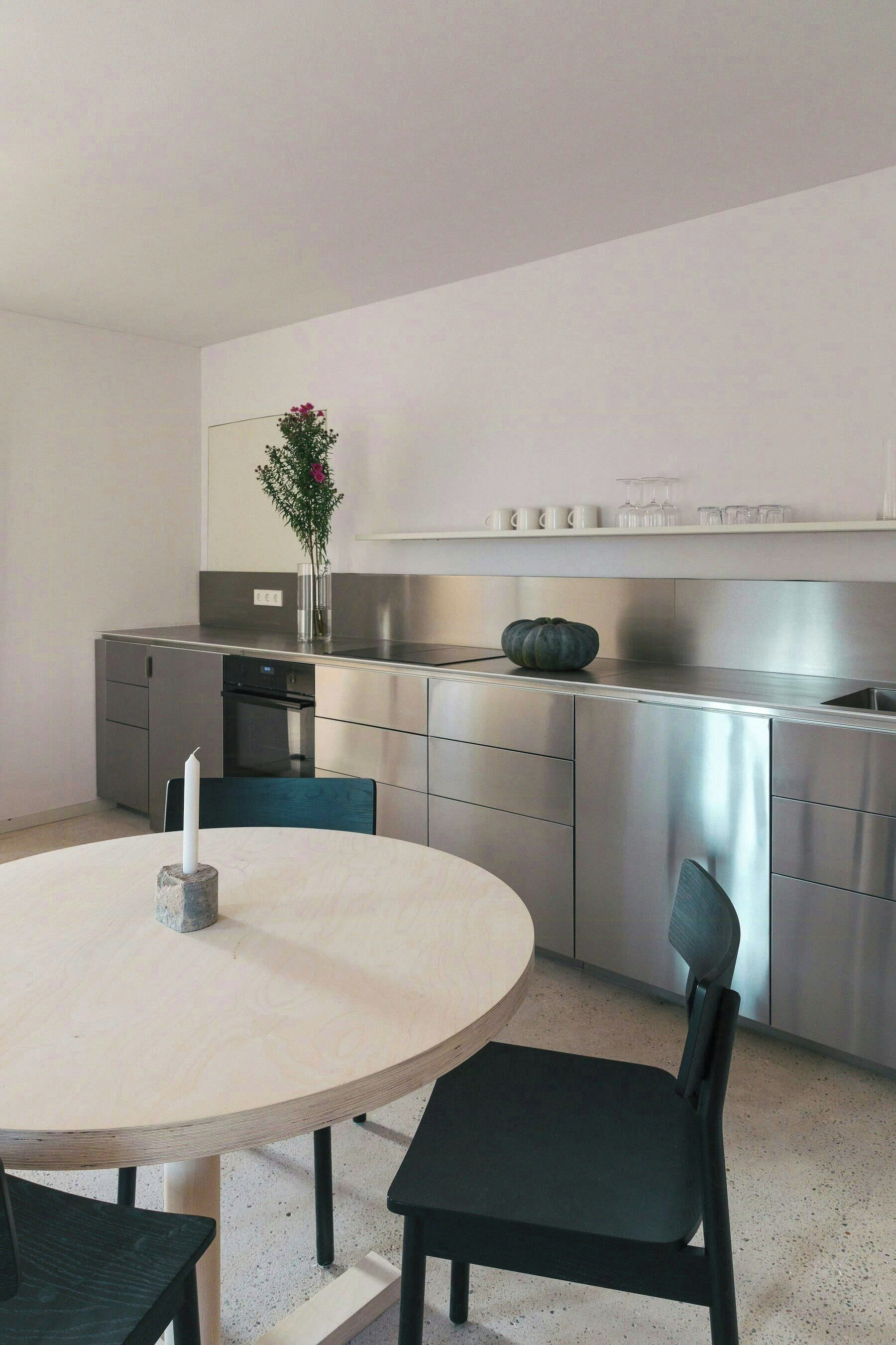 A modern kitchen with stainless steel appliances, a round dining table, and a vase with flowers.