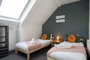 A room with two beds, a skylight, a cityscape artwork, and a side table with a lamp.