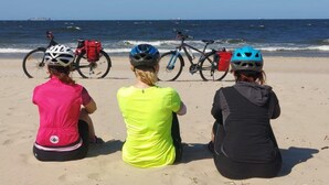 Three individuals sitting on a sandy beach with bicycles and helmets, facing the ocean. - Apartment 50 m2 for 3 People, Dziwnow (Dziwnów)