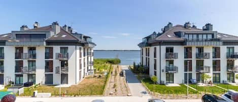 Un moderno complejo de apartamentos con vista al mar, con balcones, un estacionamiento y un camino que lleva al agua.