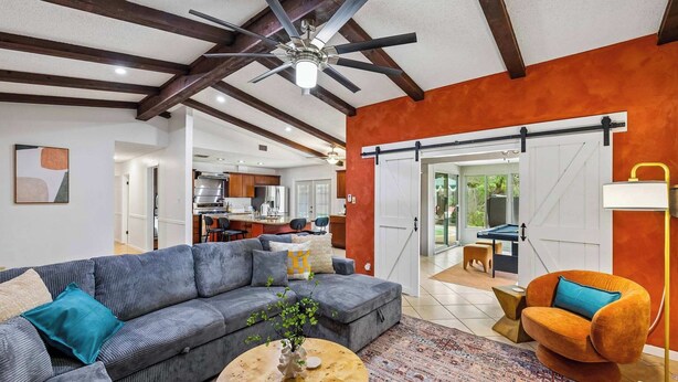A modern living room with a sectional sofa, a round coffee table, and a vibrant orange armchair. - Honky Tonk Dreams | Pool - Hot Tub - Games (San Antonio)