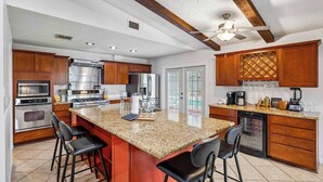 A kitchen with granite countertops, stainless steel appliances, wooden cabinets, and a bar area with stools. - Honky Tonk Dreams | Pool - Hot Tub - Games (San Antonio)