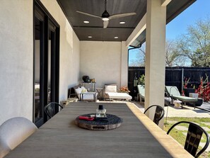 Une terrasse extérieure avec une table à manger, des chaises, un ventilateur de plafond et une vue sur le jardin.