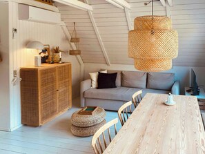 Une pièce de style loft avec une table à manger en bois, un canapé, des poufs en osier et un luminaire suspendu en rotin.