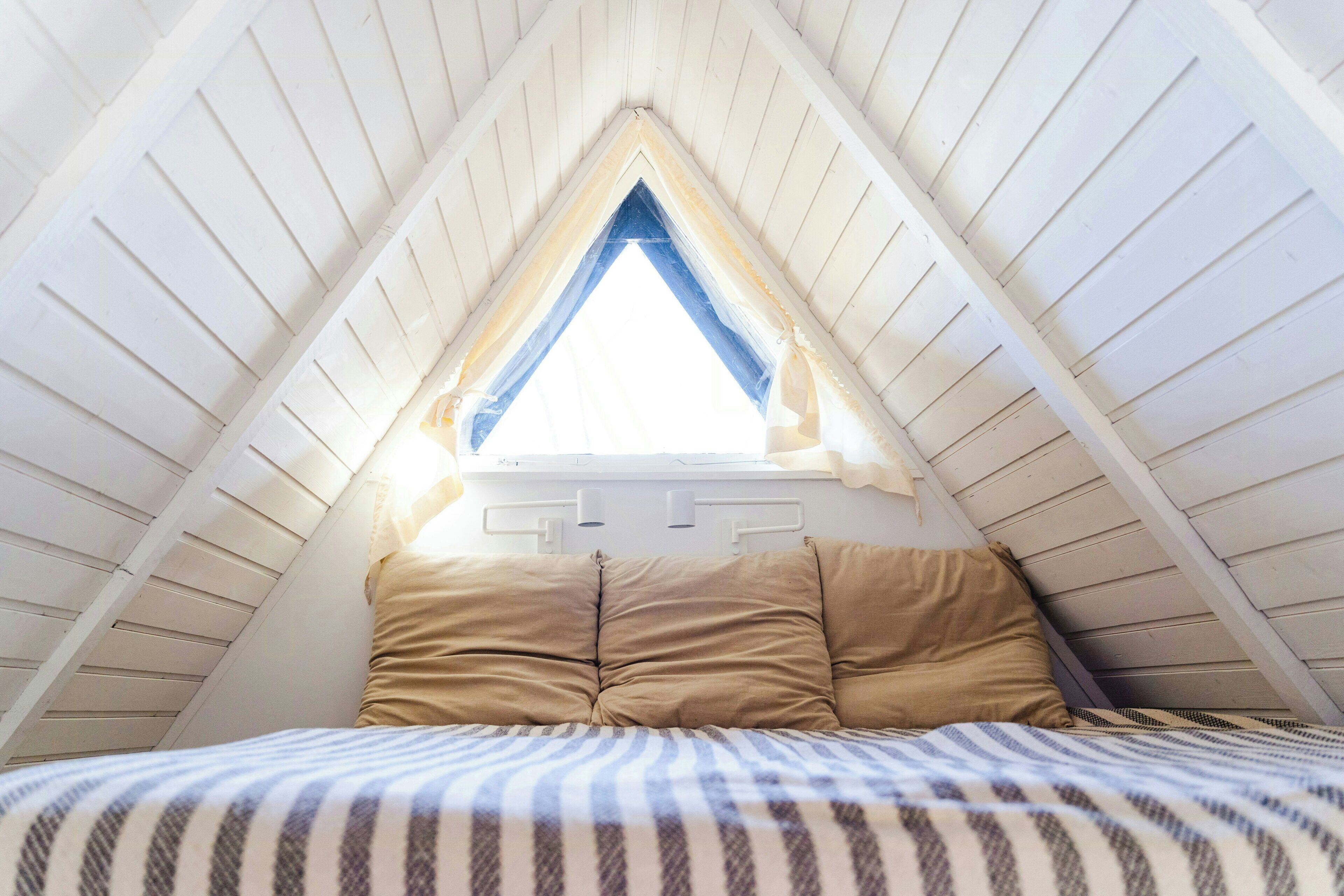 Een slaapkamer met een schuine kap, een raam en een bed met gestreepte beddengoed.