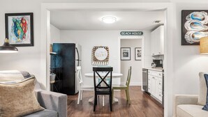 A modern kitchen with white cabinets, a dining area with a round table and chairs, and a living room with a sofa and a coffee table. - Renovated, Quick Walk to Beach + Restaurants by Tybee Cottages (Tybee Island)