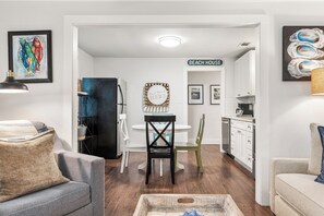 Eine moderne Küche mit weißen Schränken, ein Essbereich mit rundem Tisch und Stühlen sowie ein Wohnzimmer mit einer Couch und einem Couchtisch.