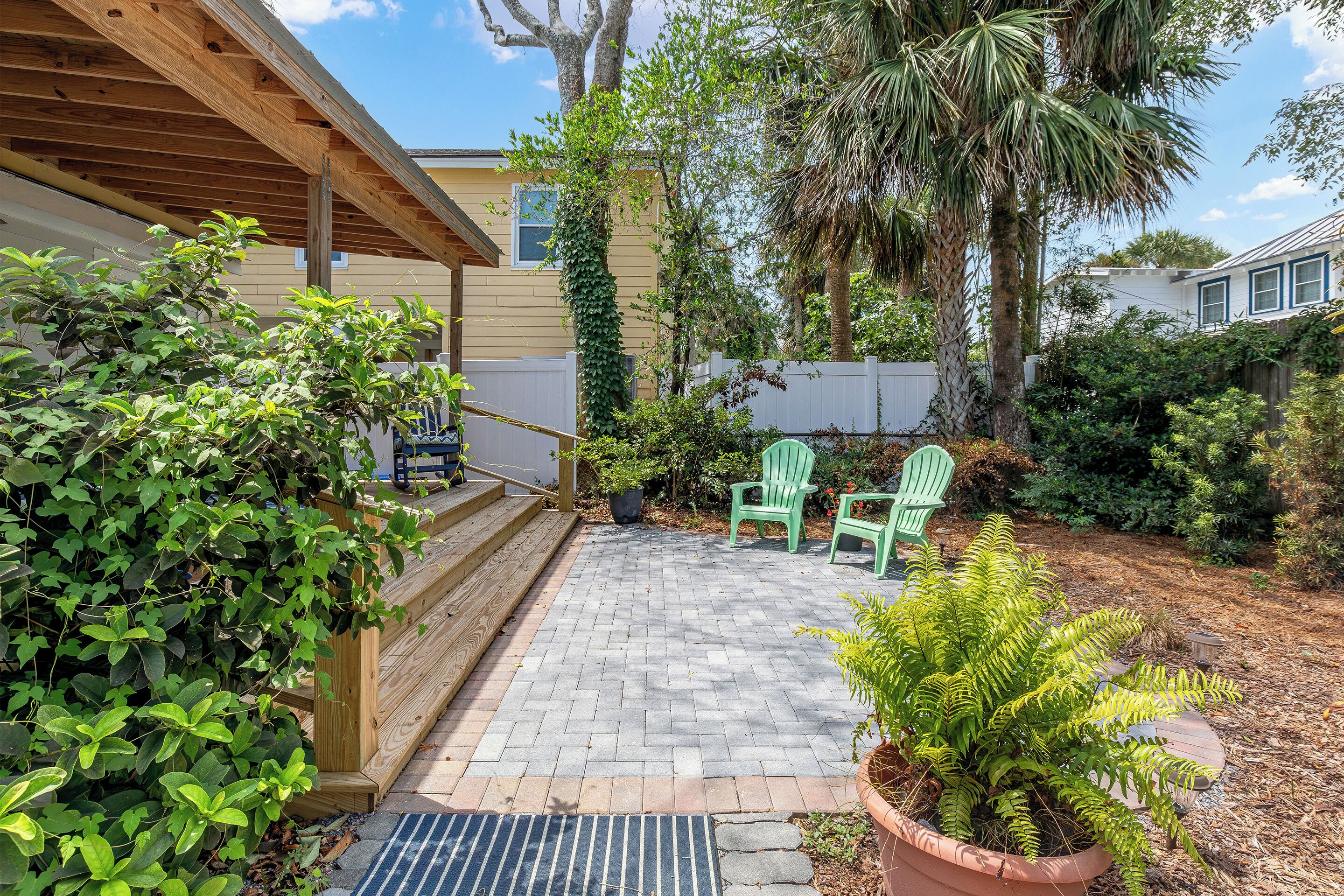 A patio area with a wooden deck, potted plants, and two green chairs.