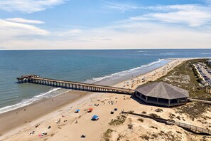 Una playa con un muelle, sombrillas y una zona de estar cubierta.