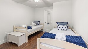 A bedroom with two single beds, a small bedside table, a ceiling fan, and a door with a mirror. - Renovated, Quick Walk to Beach + Restaurants by Tybee Cottages (Tybee Island)