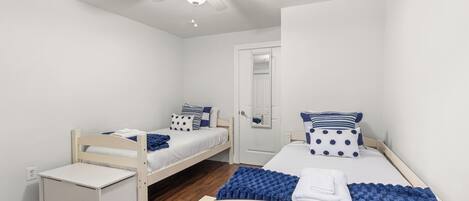 Een slaapkamer met twee eenpersoonsbedden, een klein nachtkastje, een plafondventilator en een deur met spiegel.