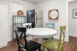 A compact kitchen with a white table, two chairs, a refrigerator, and a decorative sign. - Renovated, Quick Walk to Beach + Restaurants by Tybee Cottages (Tybee Island)