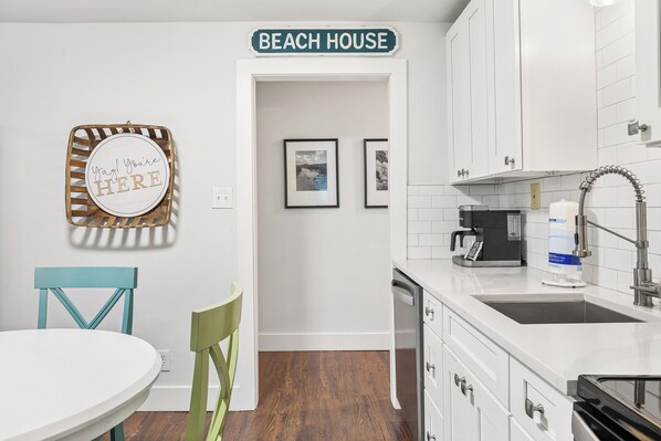 A kitchen with white cabinets, a coffee maker, and a sink. - Renovated, Quick Walk to Beach + Restaurants by Tybee Cottages (Tybee Island)