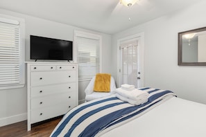 A bedroom with a bed, a television on a dresser, and a window with blinds. - Renovated, Quick Walk to Beach + Restaurants by Tybee Cottages (Tybee Island)