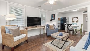 A living room with a television, wicker furniture, a ceiling fan, and a dining area with chairs and a table. - Renovated, Quick Walk to Beach + Restaurants by Tybee Cottages (Tybee Island)