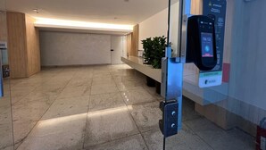 A modern reception area with a glass partition, a digital clock, and a sign indicating attention for visitors. - LK Santo Antônio 6 (Belo Horizonte)