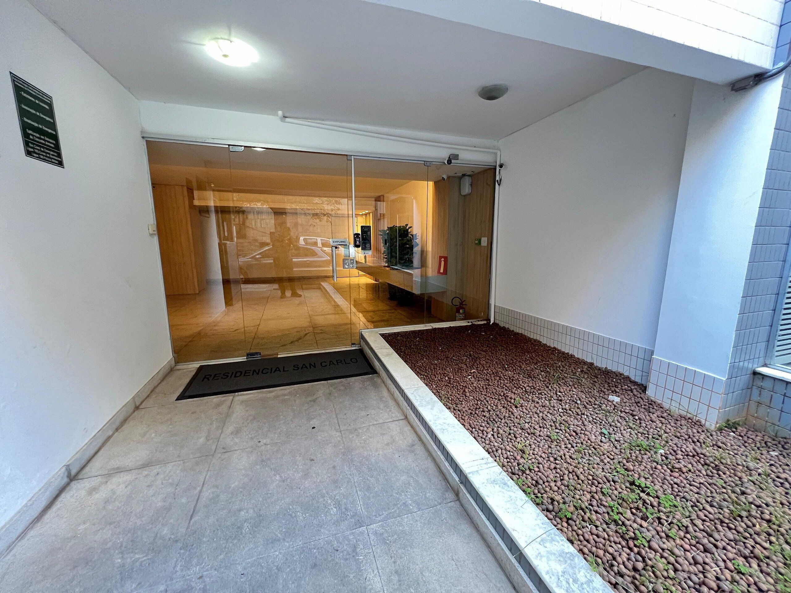 Una entrada residencial con piso de baldosas, felpudo, puerta de vidrio y un pequeño jardín con piedras.
