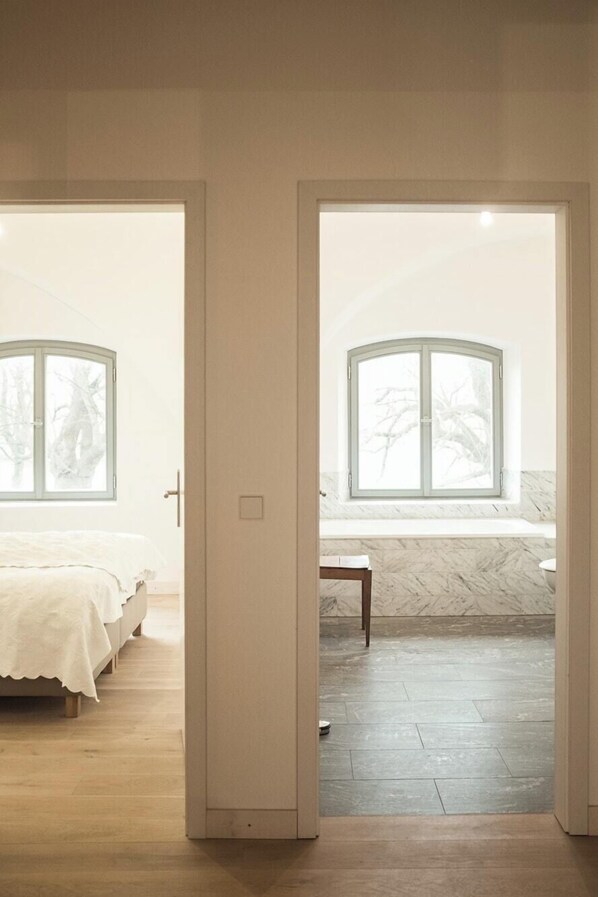A bedroom with a bed, a window, and a bathroom with a bathtub and a mirror. - Holiday apartment in manor house on Rügen (Poseritz)