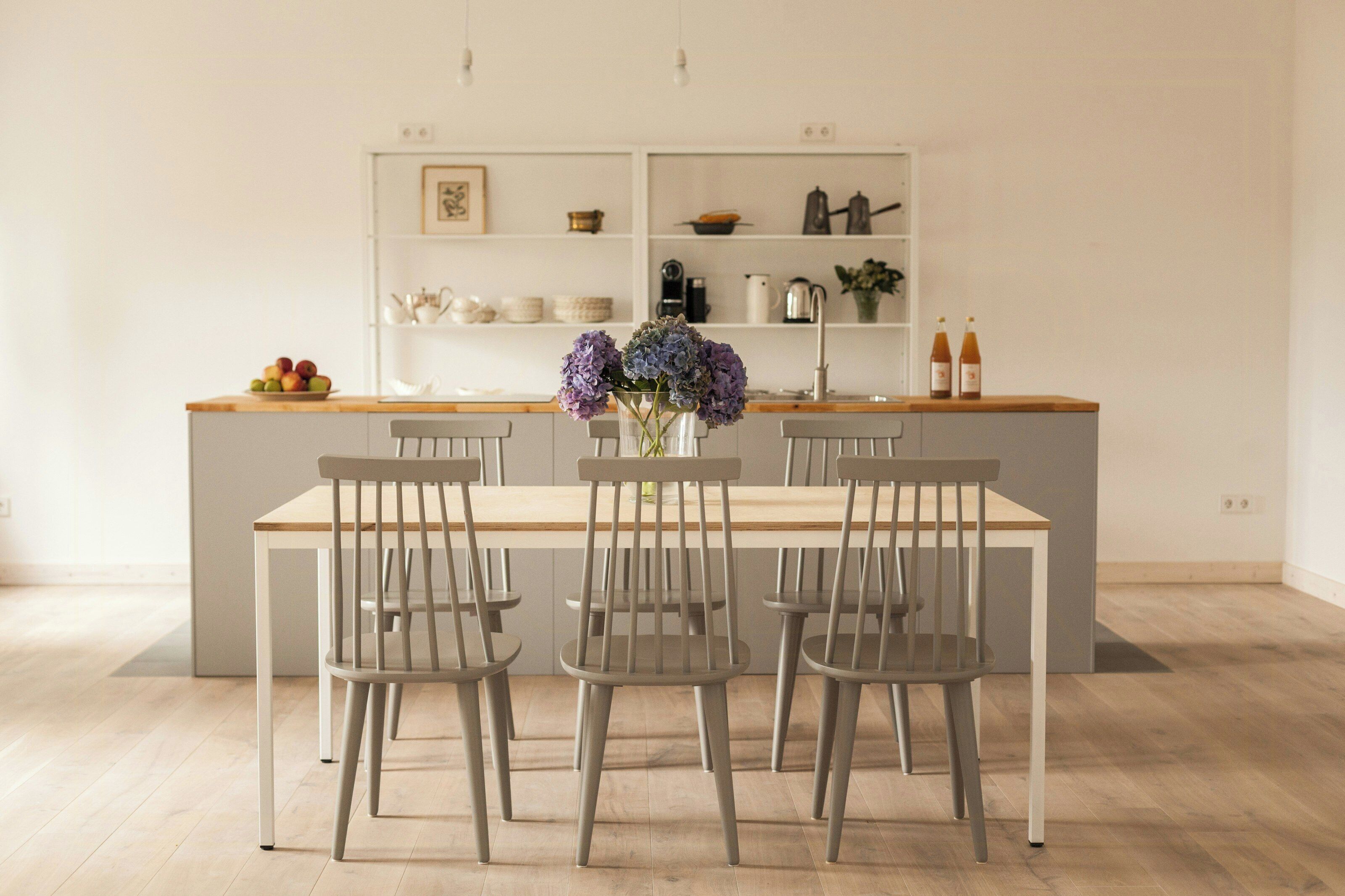 Een moderne keuken met een centraal eiland, een eettafel met stoelen en een vaas met bloemen.