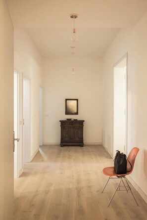 A hallway with a wooden floor, a dark wooden cabinet, a framed picture on the wall, and a red chair with a bag on it. - Holiday apartment in manor house on Rügen (Poseritz)
