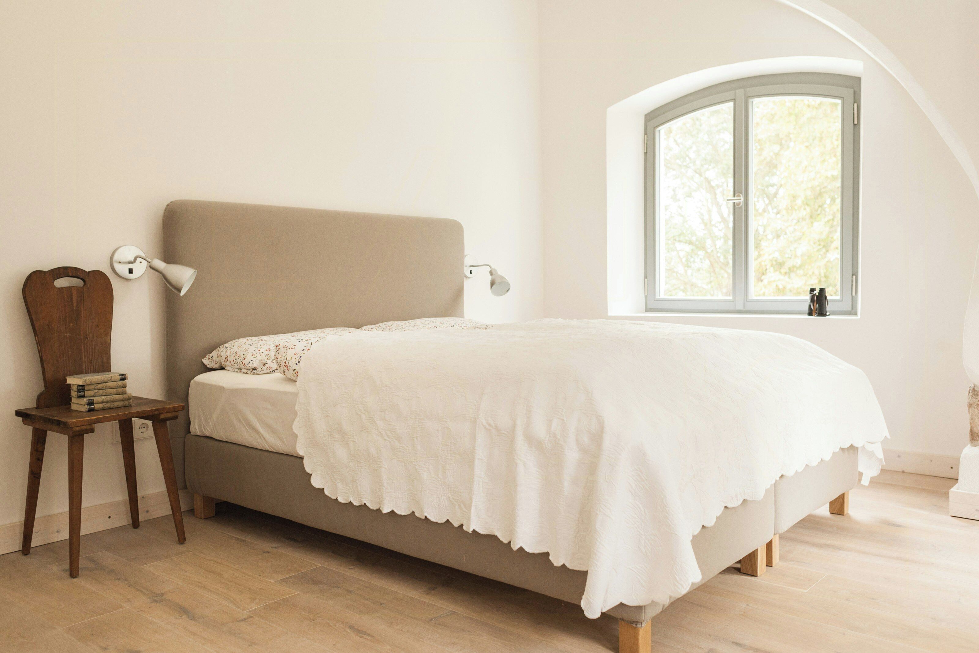 A bedroom with a bed, a nightstand, a lamp, and a window with a view.