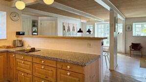Una cocina con armarios de madera, encimera de granito, iluminación colgante y vistas al comedor.