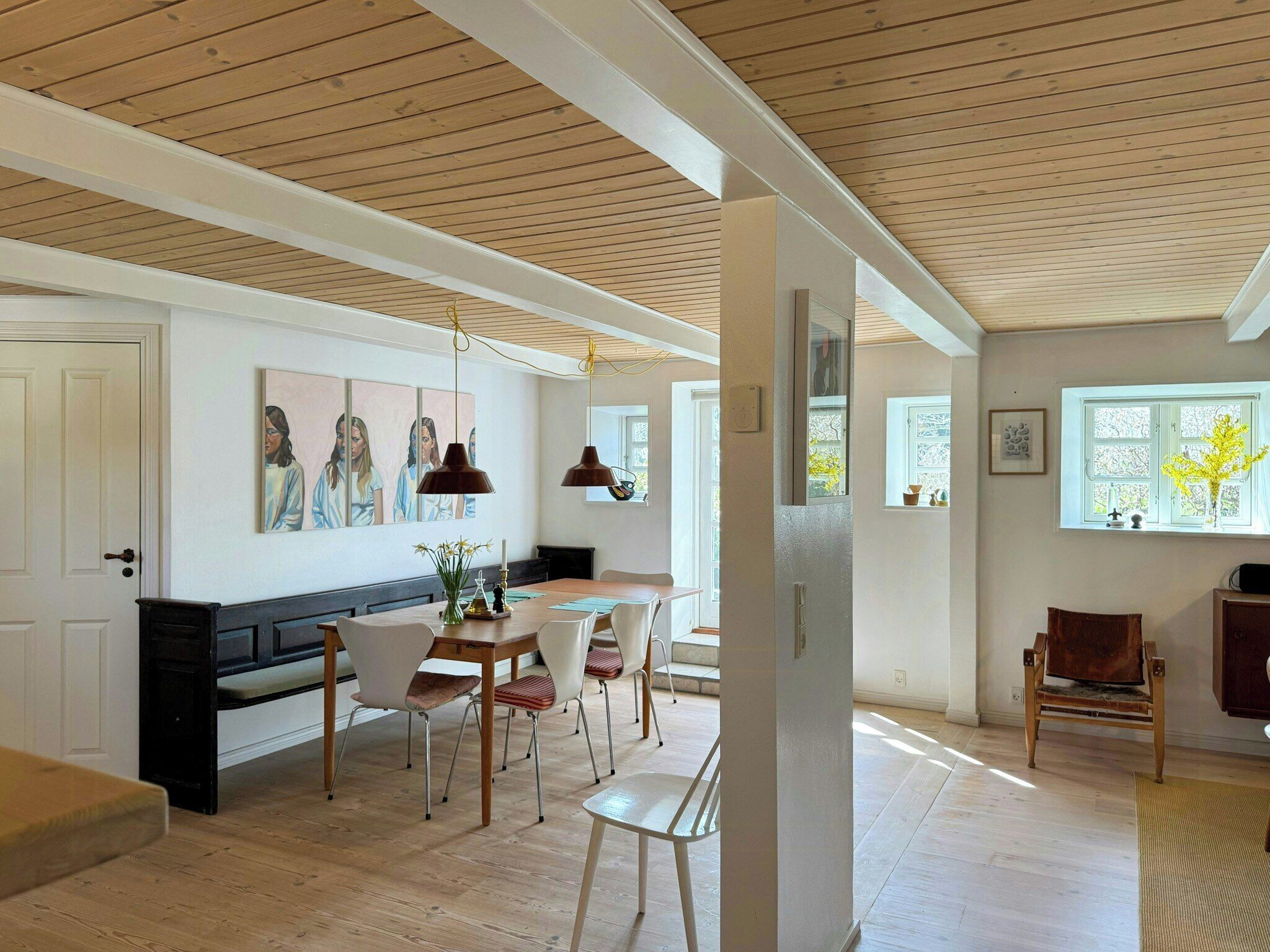 A dining area with a wooden table and chairs, a bench, pendant lights, and a painting on the wall.