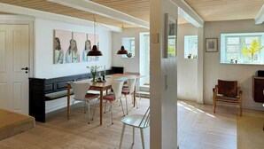 Un comedor con una mesa y sillas de madera, un banco, luces colgantes y un cuadro en la pared.