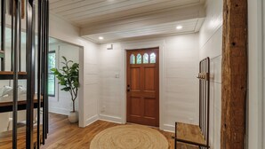 A wooden floor, a round woven rug, a wooden door, and a potted plant.