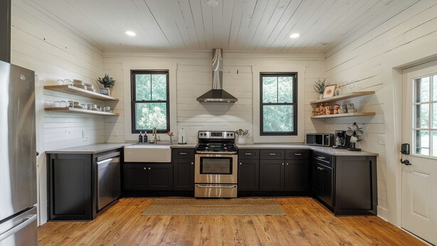 A modern kitchen with wooden floors, stainless steel appliances, and black cabinetry.
