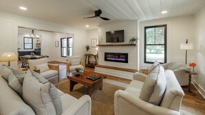 A spacious living area with a fireplace, a dining area, and a kitchen visible through an open door.