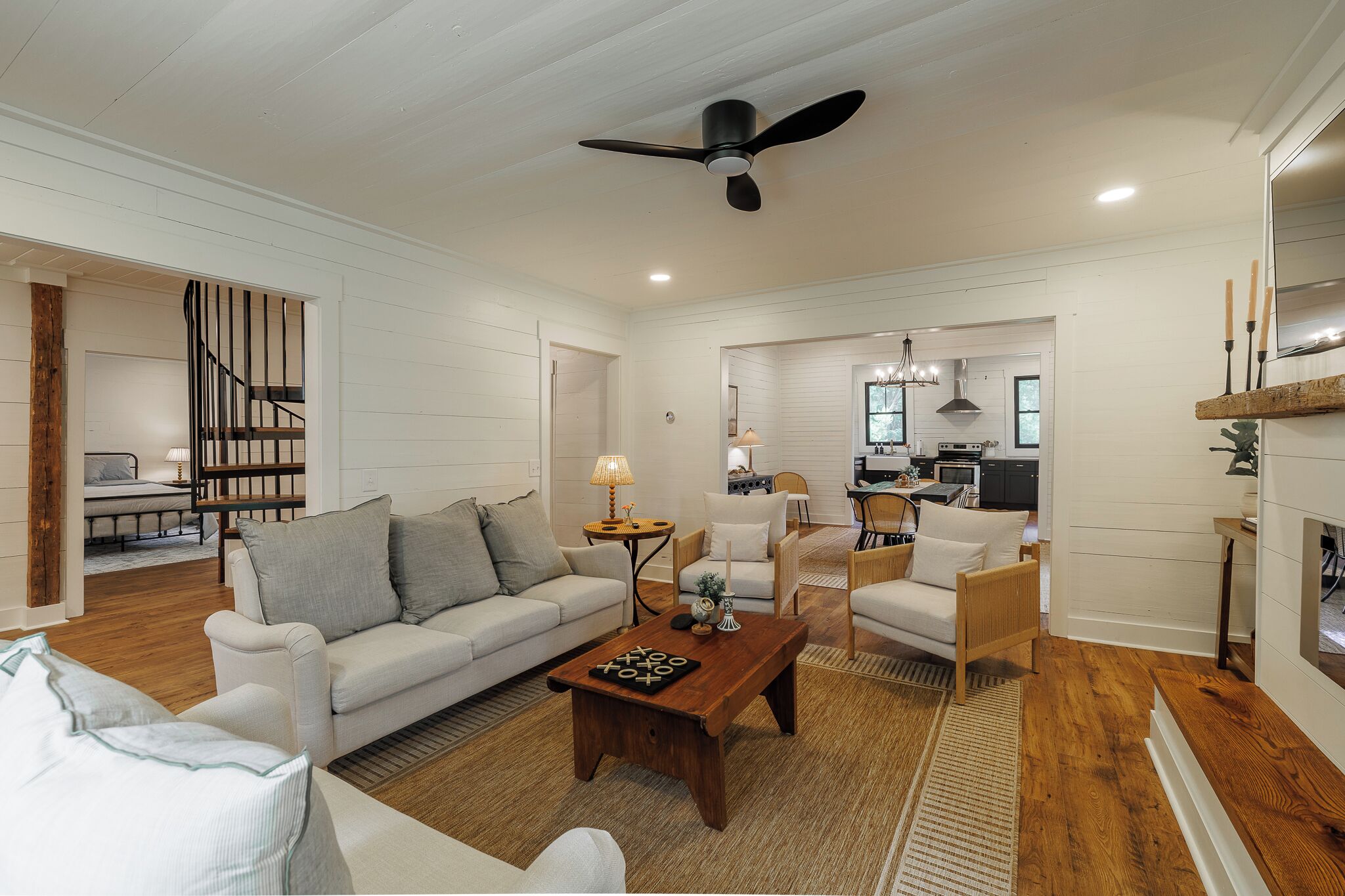 Un salon spacieux comprenant un canapé, des fauteuils, une table basse et un ventilateur de plafond.