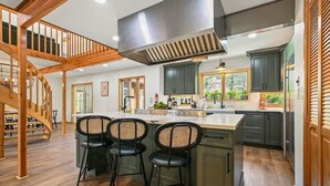 A kitchen with a central island, dark cabinets, and a wooden staircase.