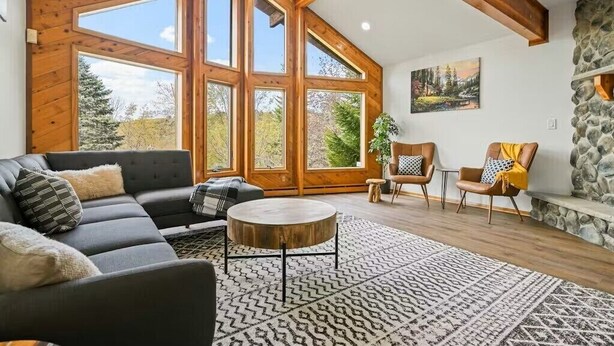 A spacious living room with a large sofa, a round coffee table, and two armchairs. Large windows provide a view of the outdoors.