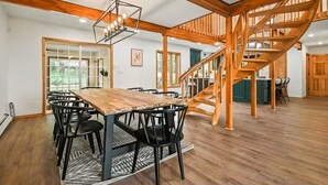 A spacious dining area with a wooden table and chairs, a staircase, and a view of the outdoors.