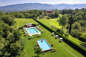 A pool area with a rectangular pool, lounge chairs, and umbrellas, surrounded by well-manicured lawns and trees, with a mountain backdrop. - Dog-friendly barn with views in Reggello (Reggello)