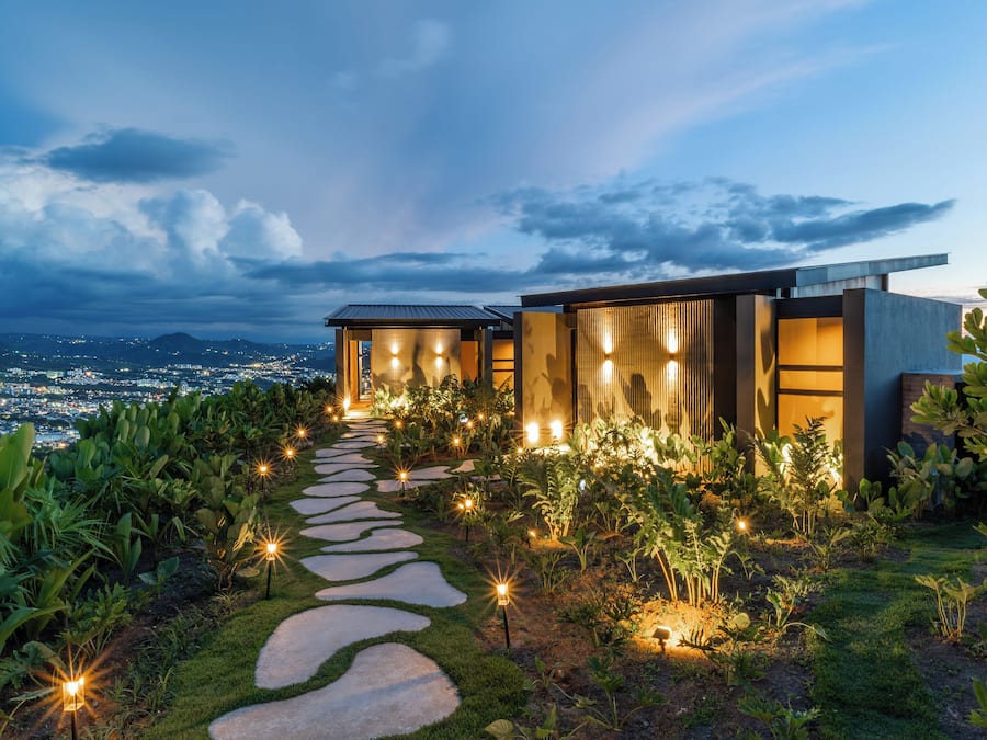 Una casa moderna con un camino de piedra que conduce a la entrada, rodeada de exuberante vegetación.