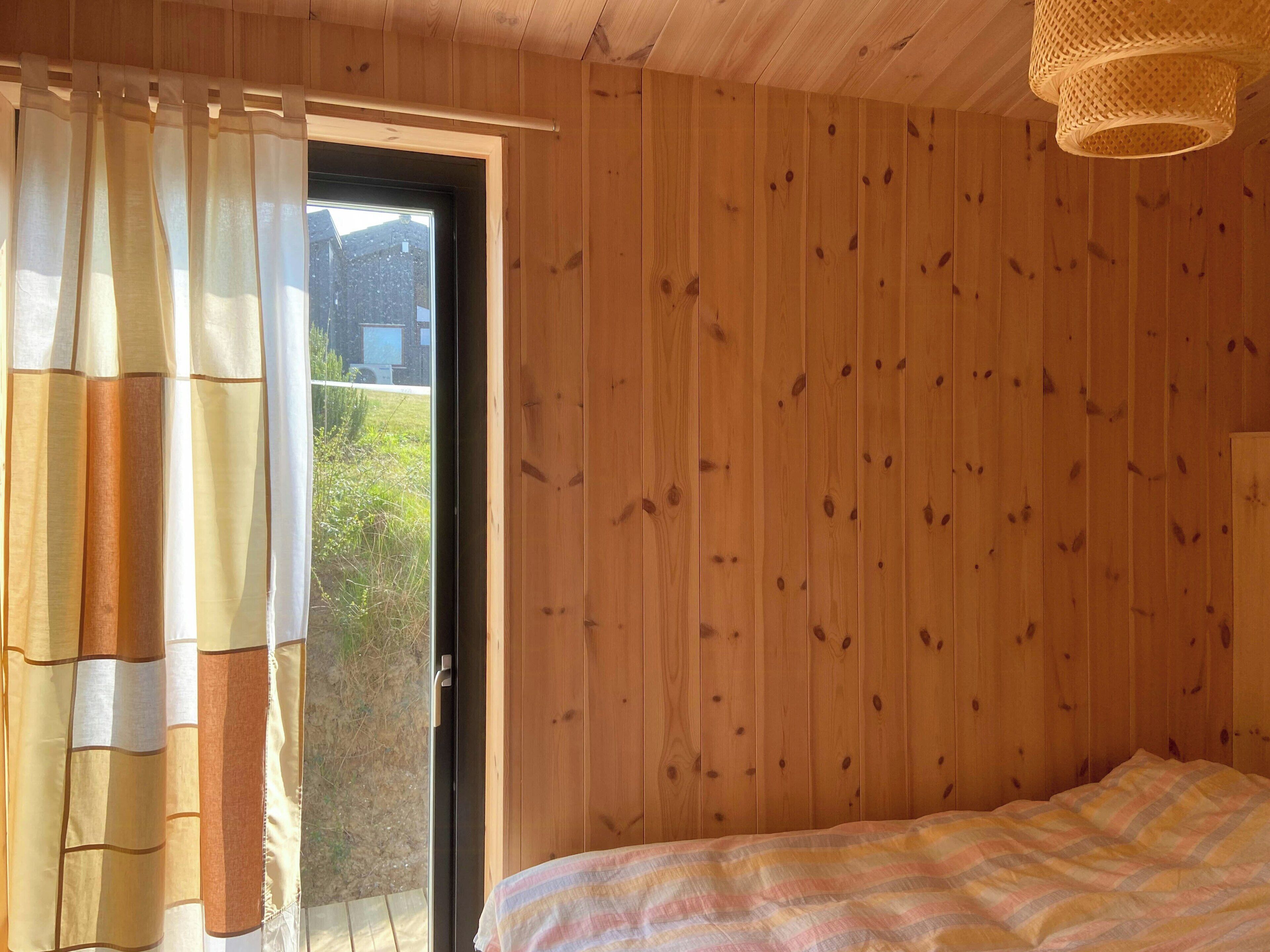 Una stanza in legno con un letto, una porta che dà all'esterno e una finestra con tende.