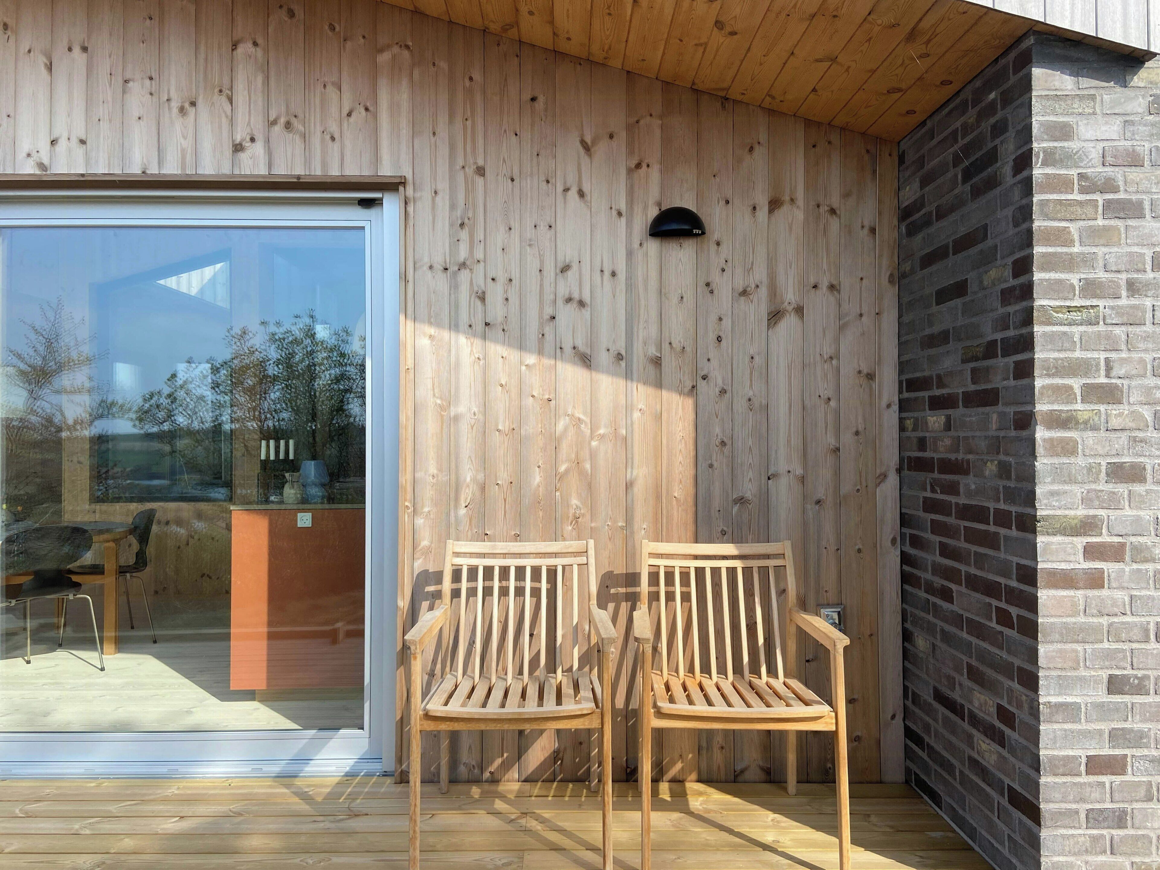 A wooden exterior wall, a glass door, and two wooden chairs on a deck.
