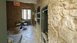 A stone-walled room with a dining table and chairs, a hanging light fixture, and a window with natural light. - DOMUS GABRIEL (Giovinazzo)